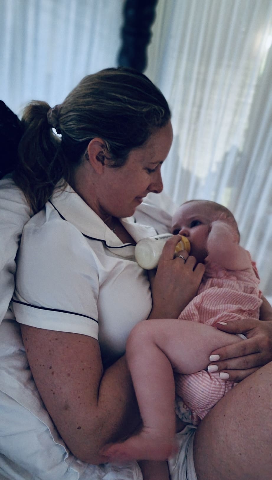Tired new mother sitting on couch holding baby looking overwhelmed in early postpartum